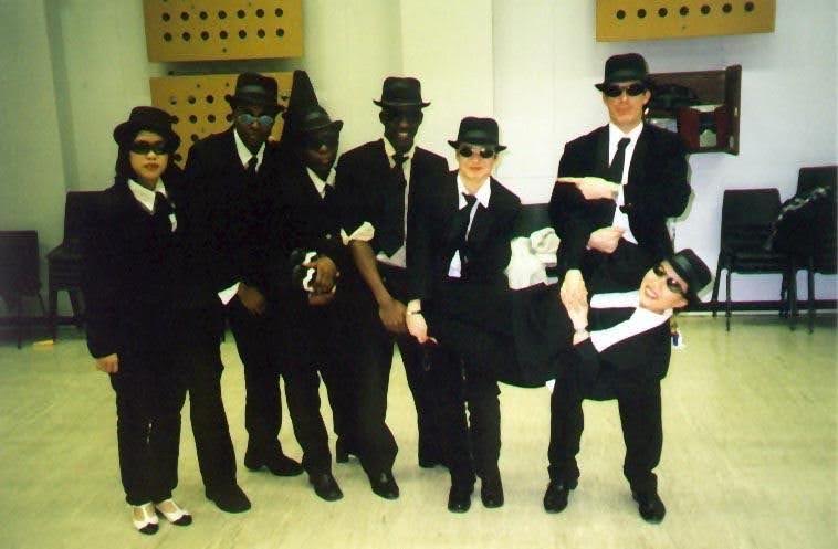 Group of swing dancers in black suits and hats posing indoors for an LSE Swing Dance Society performance. Apr 2000 student performance at the LSE’s global show.