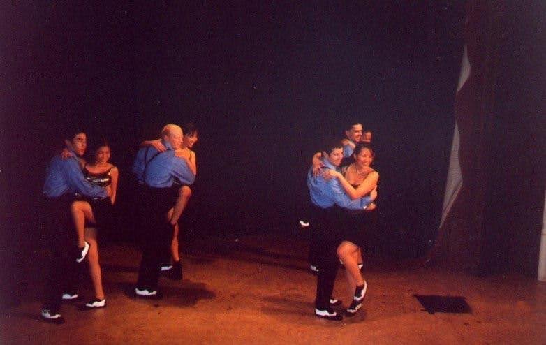 Swing dance couples performing a partnered routine onstage in blue shirts and black trousers.